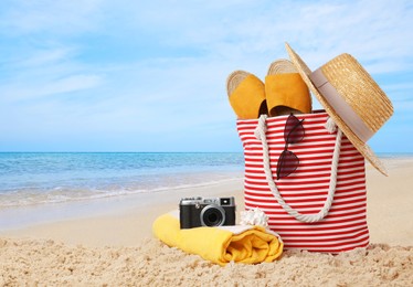 Image of Stylish bag with different accessories on sandy beach near ocean. space for text 
