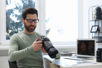 Professional photographer in glasses holding digital camera at table in office, space for text