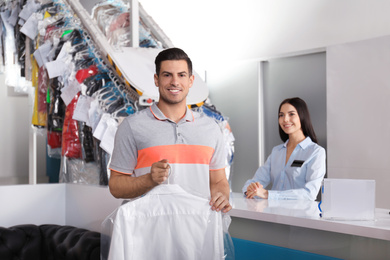 Happy client with shirt near counter at dry-cleaner's