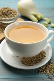 Photo of Fennel tea in cup, seeds and fresh vegetable on light blue wooden table, closeup