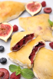 Delicious samosas, berries, mint leaves and fig on white tiled table, closeup