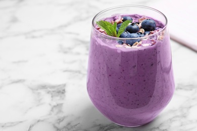 Glass of delicious blueberry smoothie with granola and mint on white marble table. Space for text