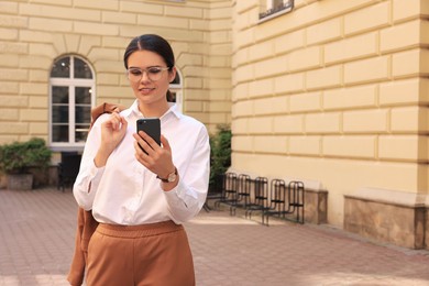 Photo of Beautiful young woman using smartphone near building outdoors
