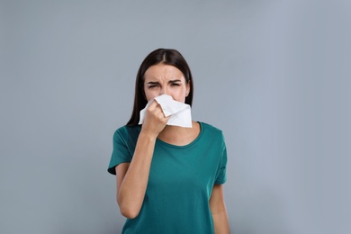 Young woman suffering from allergy on grey background