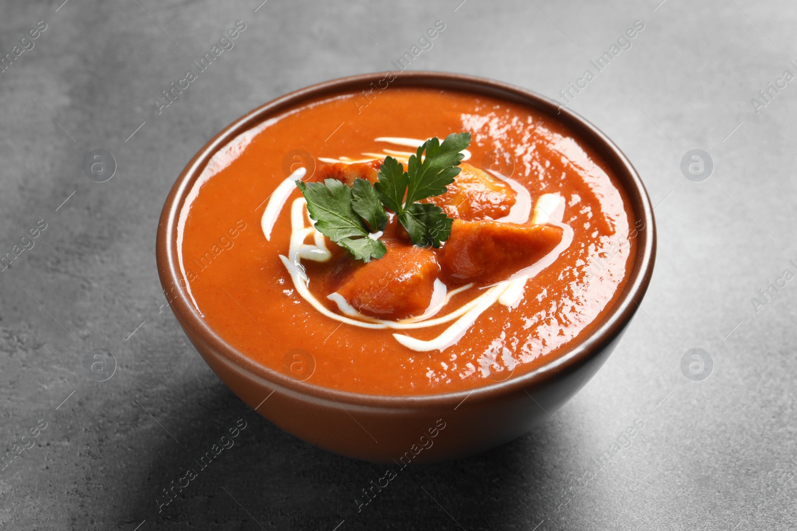 Photo of Bowl of delicious butter chicken on grey table. Traditional indian Murgh Makhani