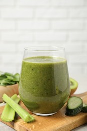 Photo of Delicious green juice and fresh ingredients on wooden board against brick wall, closeup