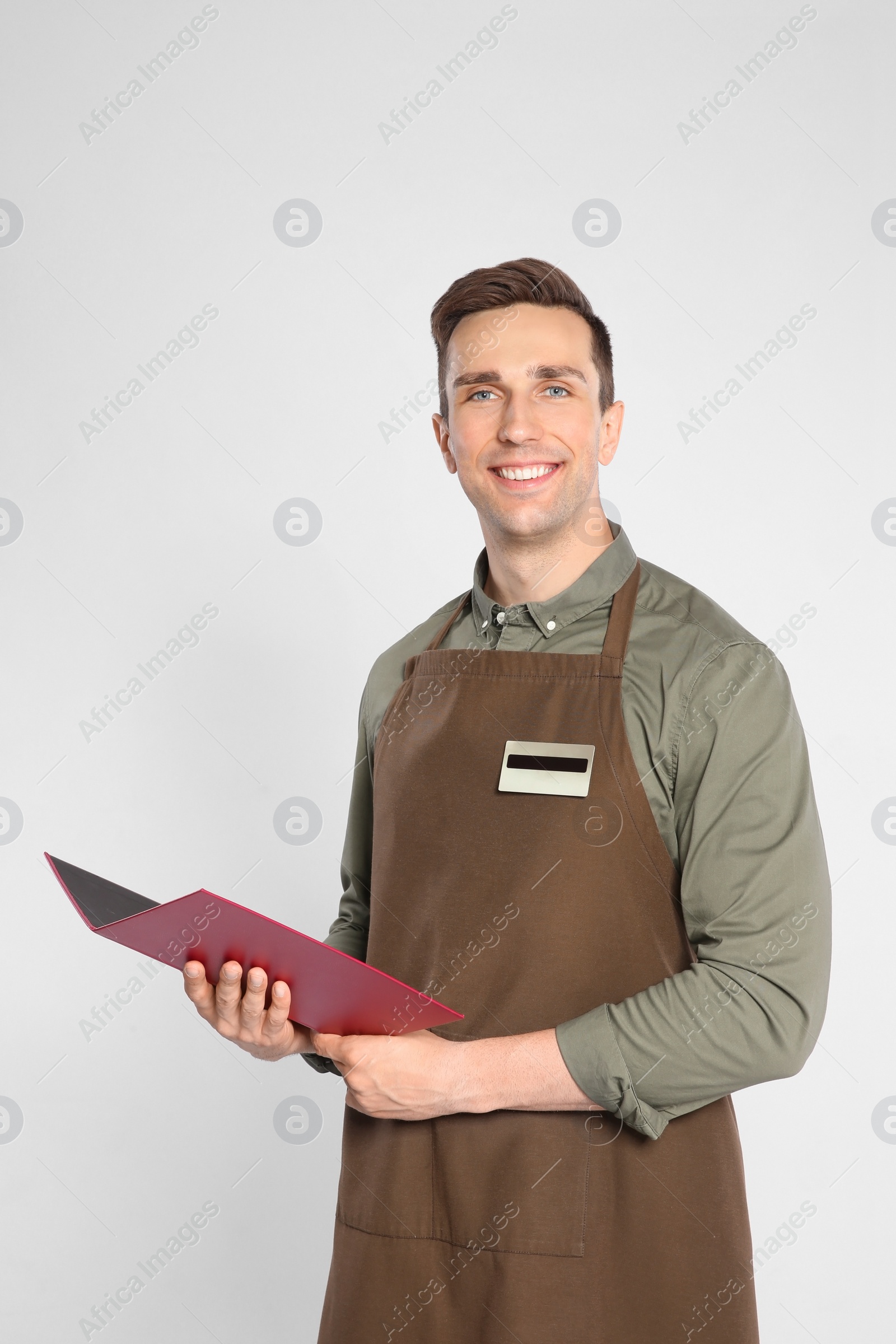 Photo of Handsome waiter in apron with menu on light background