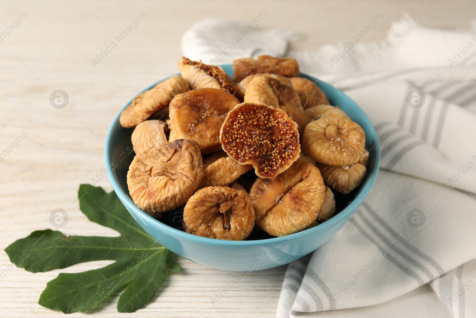 Photo of Bowl with tasty dried figs and green leaf on white wooden table