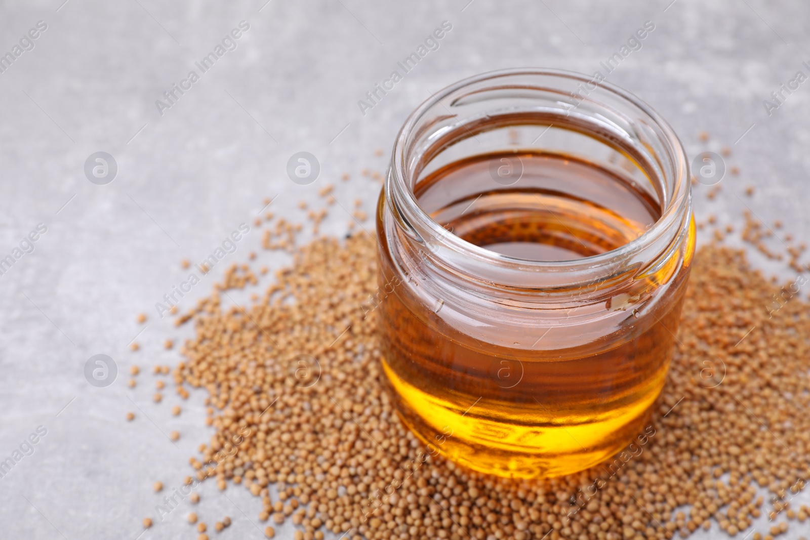 Jar of natural oil and mustard seeds on light grey table. Space for text Photo of Jar of natural oil and mustard seeds on light grey table. Space for text