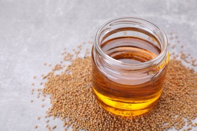 Photo of Jar of natural oil and mustard seeds on light grey table. Space for text