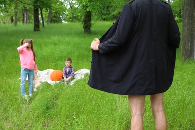 Male exhibitionist opening his coat in front of kids outdoors. Child in danger