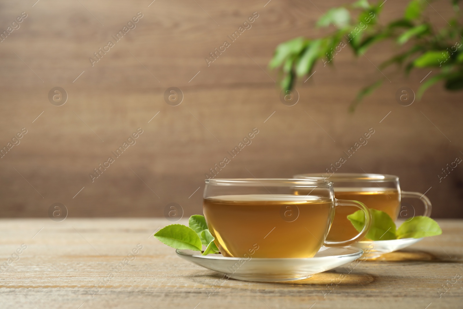 Photo of Cups of green tea and leaves on wooden table. Space for text