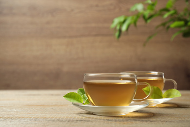 Photo of Cups of green tea and leaves on wooden table. Space for text