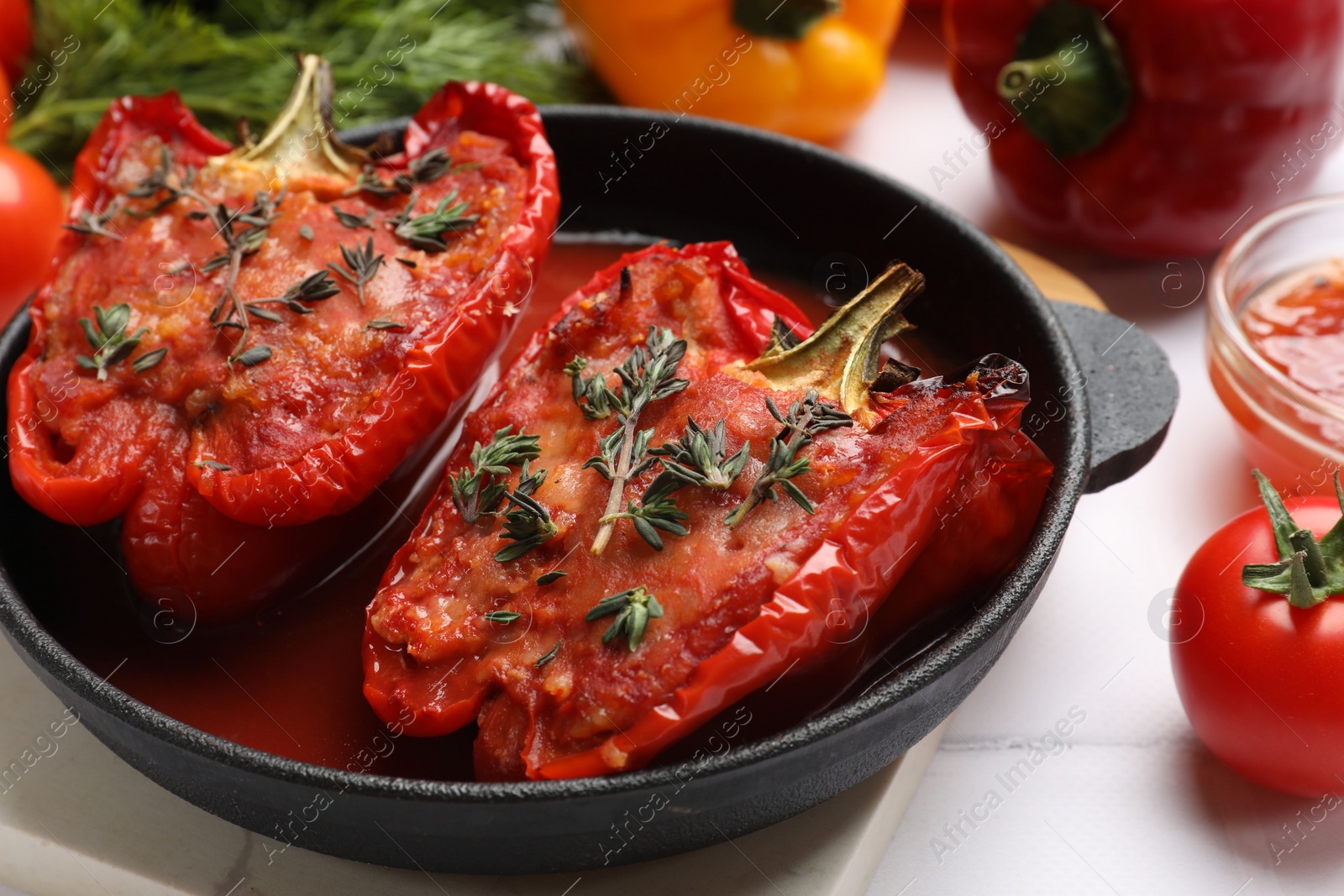 Photo of Tasty stuffed peppers in dish and ingredients on white tiled table, closeup