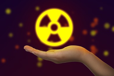 Image of Woman holding glowing radiation warning symbol on dark background, closeup