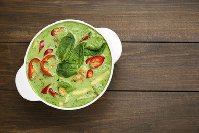 Saucepan with delicious green curry chicken soup on wooden table, top view. Space for text