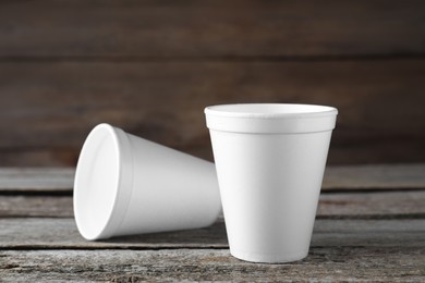 Two white styrofoam cups on wooden table, closeup