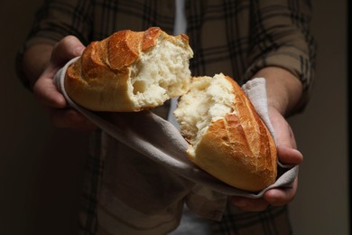 Photo of Man breaking loaf of fresh bread on dark background, closeup