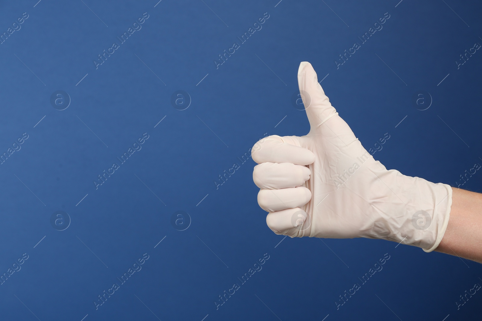 Photo of Person in medical gloves showing thumb up on blue background, closeup of hand. Space for text
