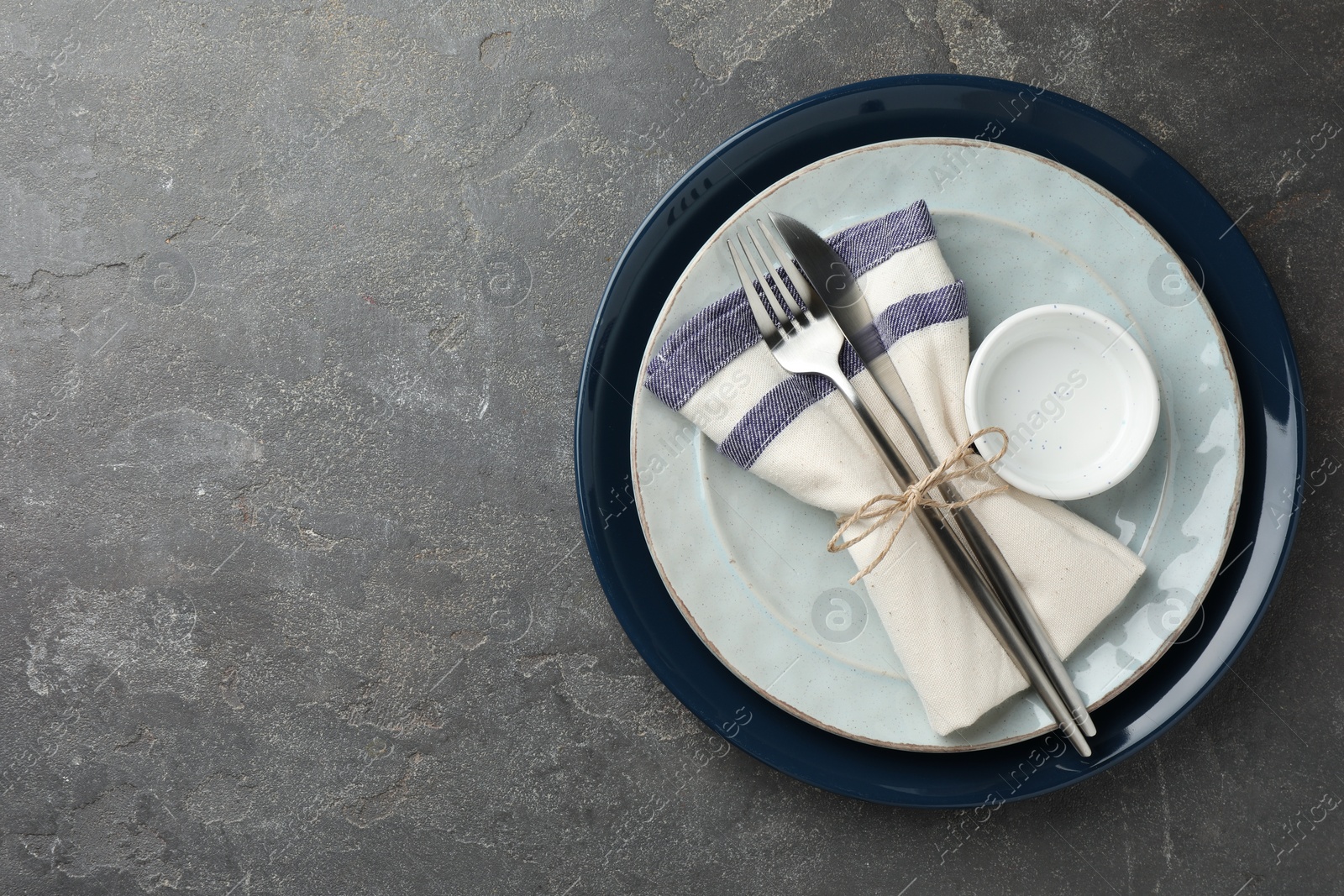 Photo of Stylish setting with cutlery, plates, bowl and napkin on grey textured table, top view. Space for text