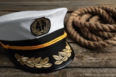 Photo of Peaked cap with accessories and rope on wooden background, closeup