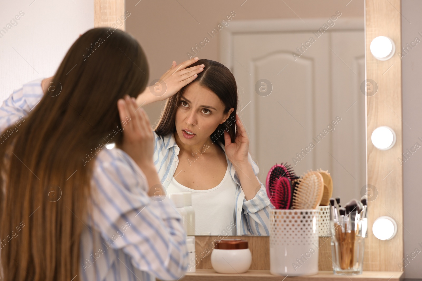 Photo of Young woman with hair loss problem looking in mirror indoors