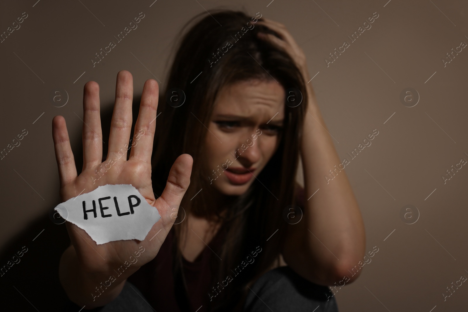 Photo of Abused young woman with sign HELP near beige wall, focus on hand. Domestic violence concept