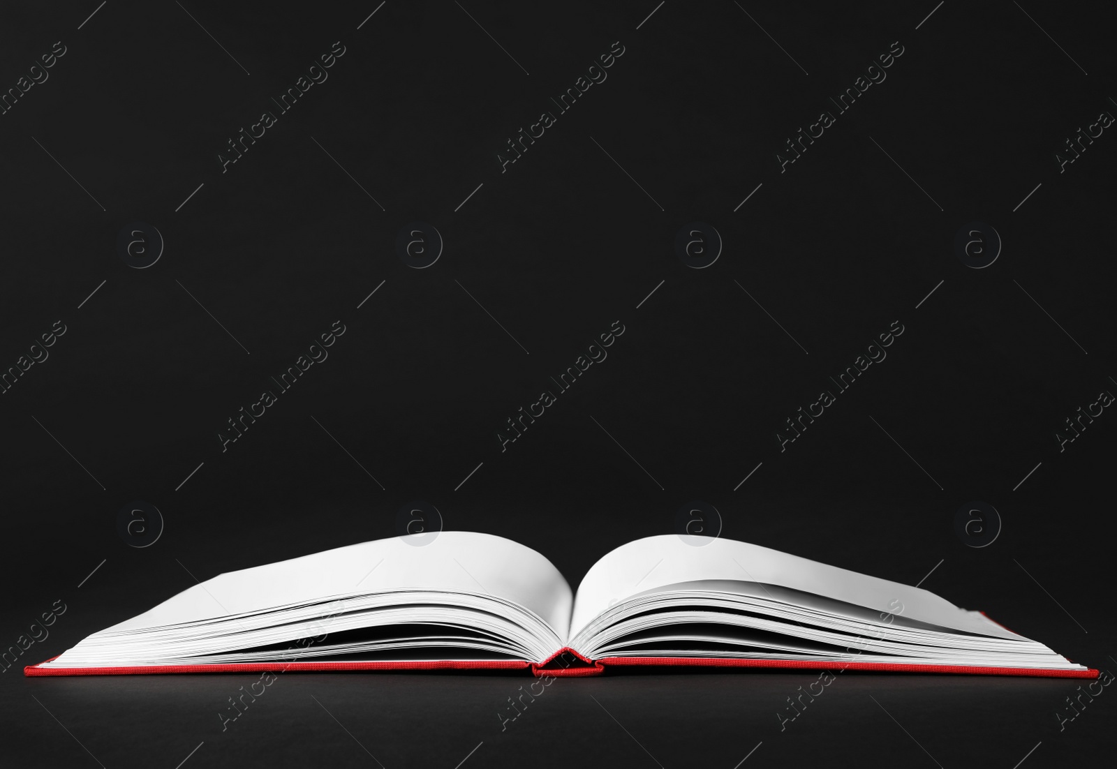 Photo of Open book with red cover on black background. Space for text