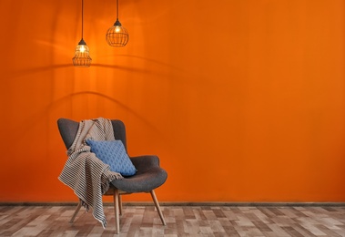 Photo of Armchair with pillow and plaid near color wall in room