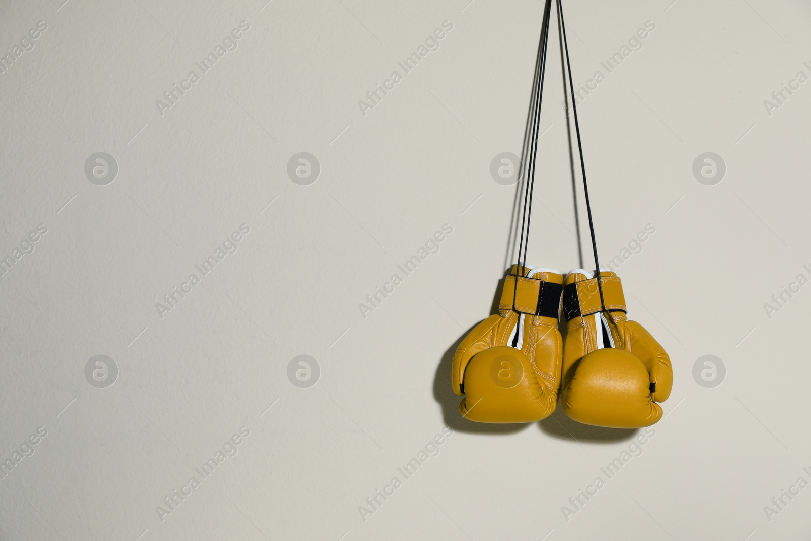 Image of Pair of yellow boxing gloves hanging on light grey wall, space for text