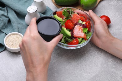 Woman adding soy sauce to tasty salad at grey table, closeup