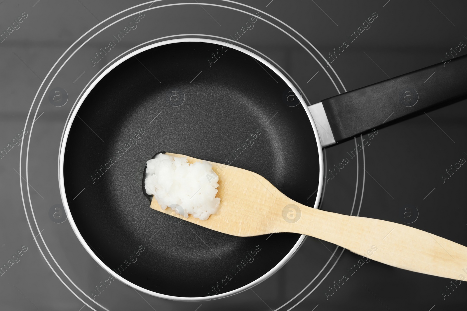 Photo of Frying pan with coconut oil and wooden spatula on induction stove, top view. Healthy cooking