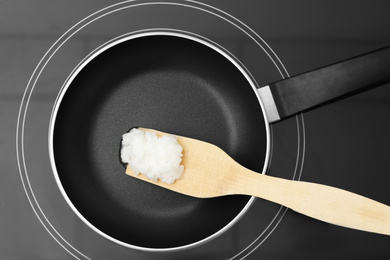 Photo of Frying pan with coconut oil and wooden spatula on induction stove, top view. Healthy cooking