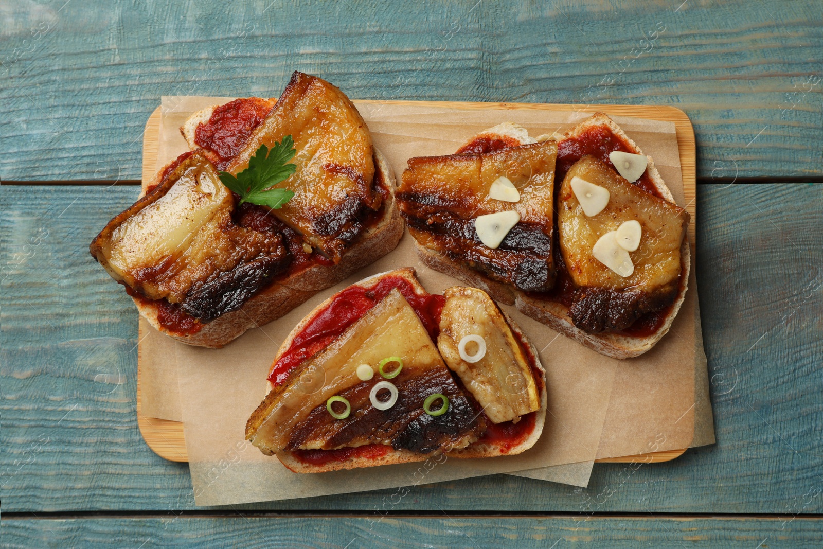 Photo of Tasty sandwiches with fried pork fatback slices on light blue wooden table, top view