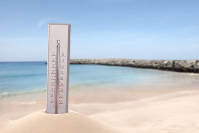 Image of Thermometer in sand near sea showing temperature, summer weather