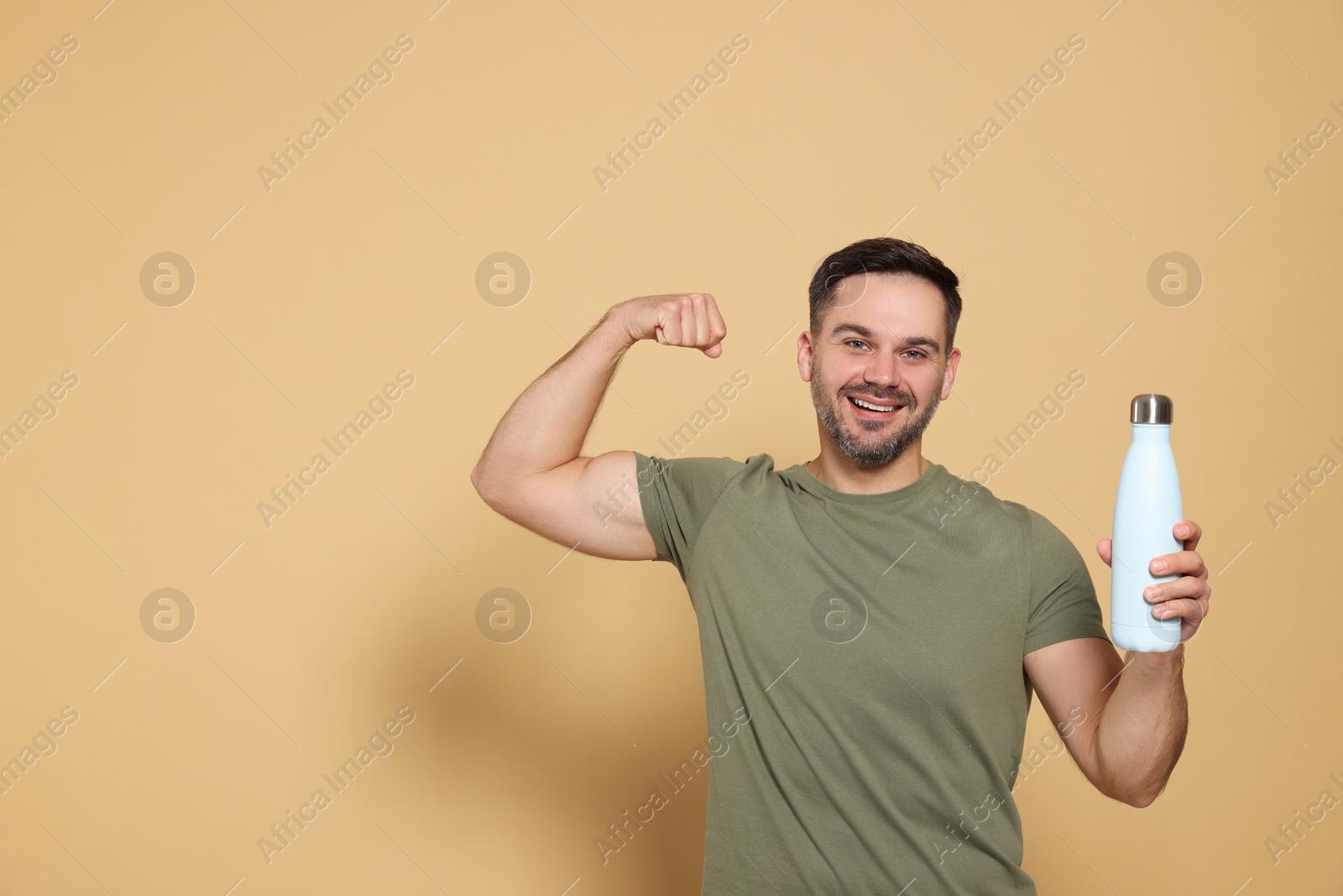 Photo of Happy man holding thermo bottle and showing arm on beige background, space for text