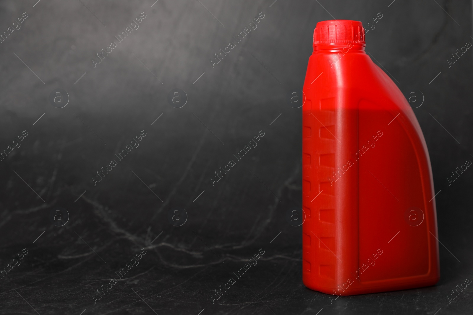 Photo of Motor oil in red canister on black background, space for text