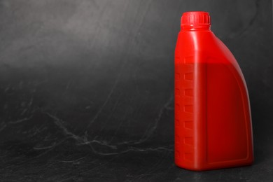 Photo of Motor oil in red canister on black background, space for text
