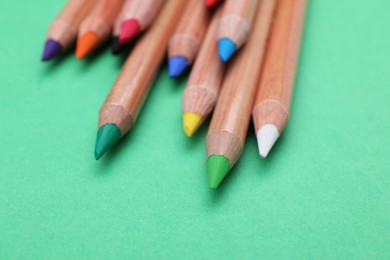 Many colorful pastel pencils on light green background, closeup. Drawing supplies