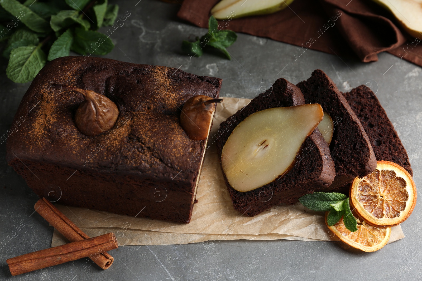 Photo of Tasty pear bread with cinnamon, mint and dried orange slices on grey table. Homemade cake