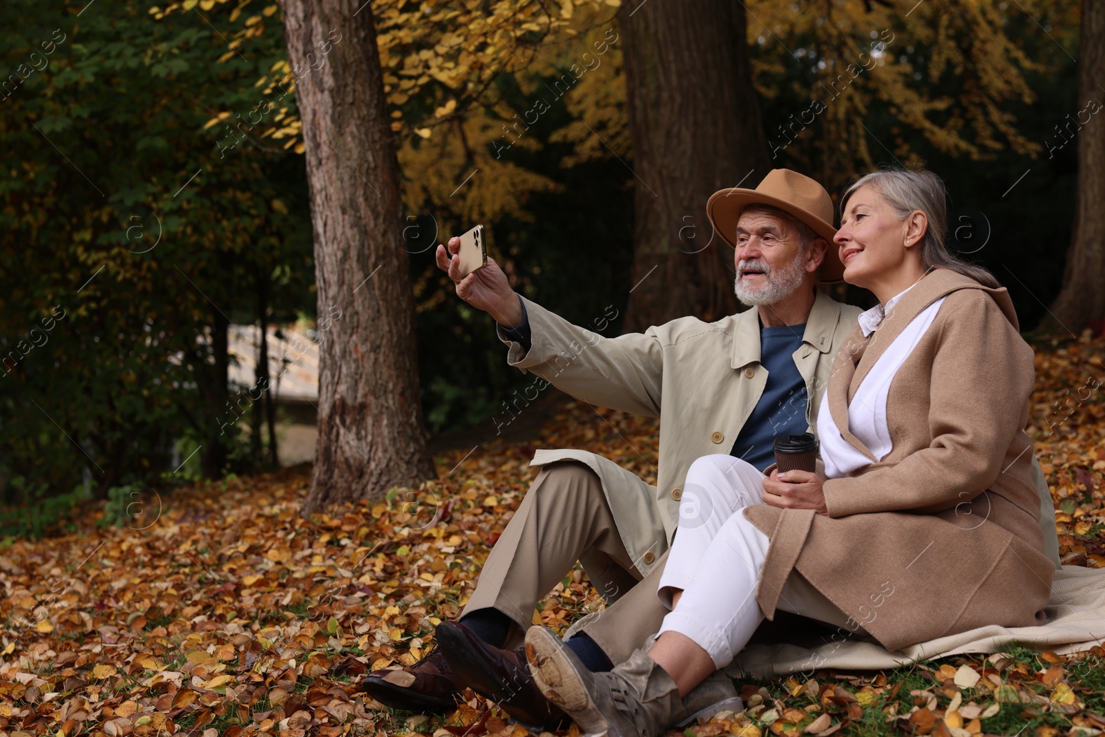 Photo of Affectionate senior couple taking selfie on blanket in autumn park
