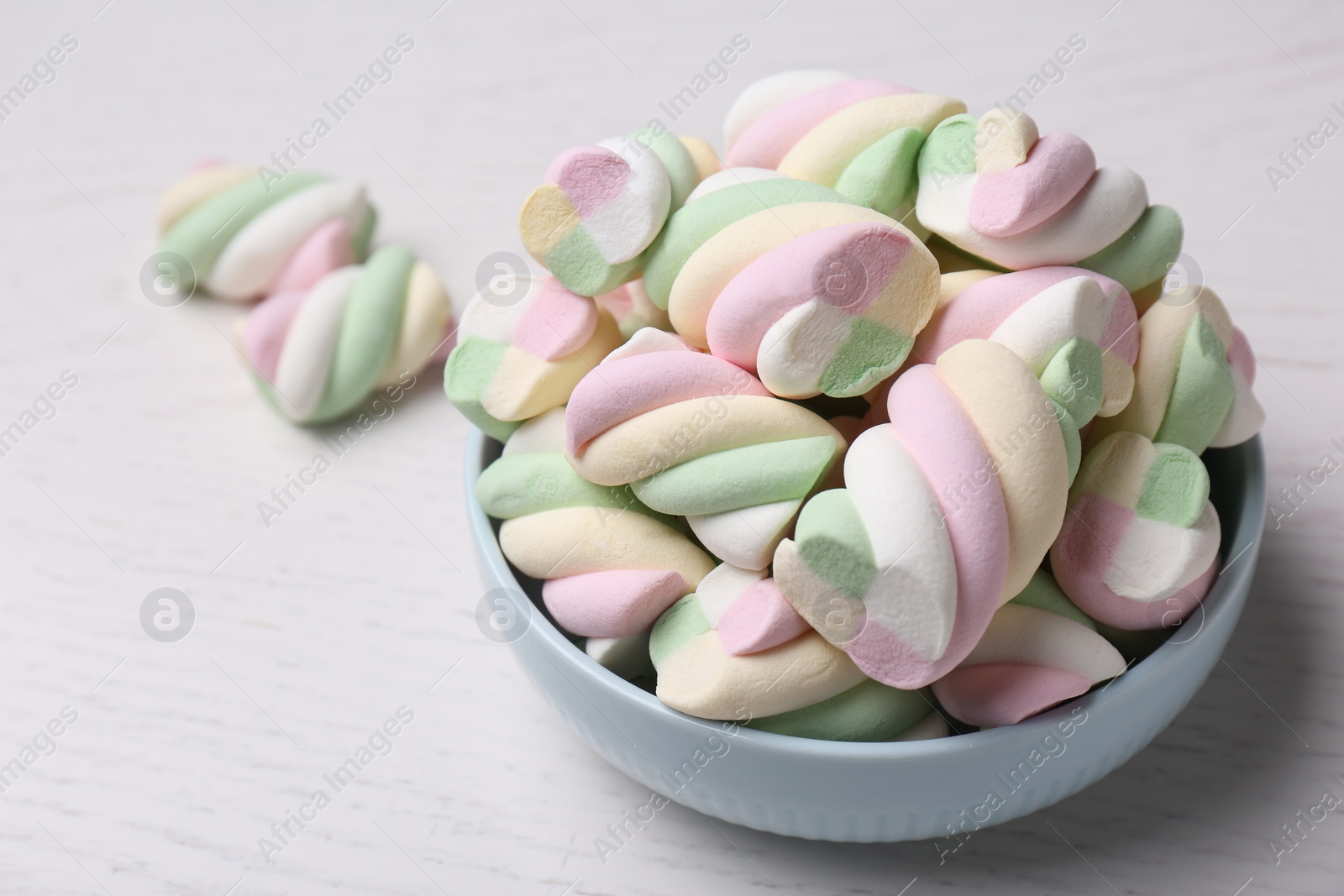 Photo of Bowl with colorful marshmallows on white table, closeup. Space for text