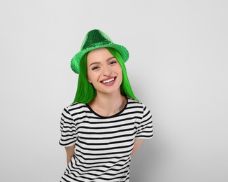 Image of St. Patrick's day party. Pretty woman with green hair and leprechaun hat on light background
