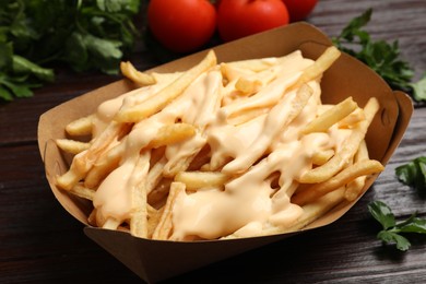 Photo of Tasty potato fries, cheese sauce in paper container and products on wooden table, closeup