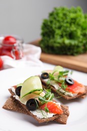 Photo of Tasty rye crispbreads with salmon, cream cheese and vegetables on plate, closeup