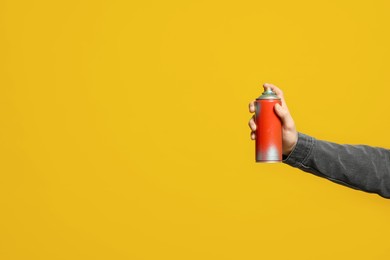 Photo of Man holding can of spray paint on yellow background, closeup. Space for text