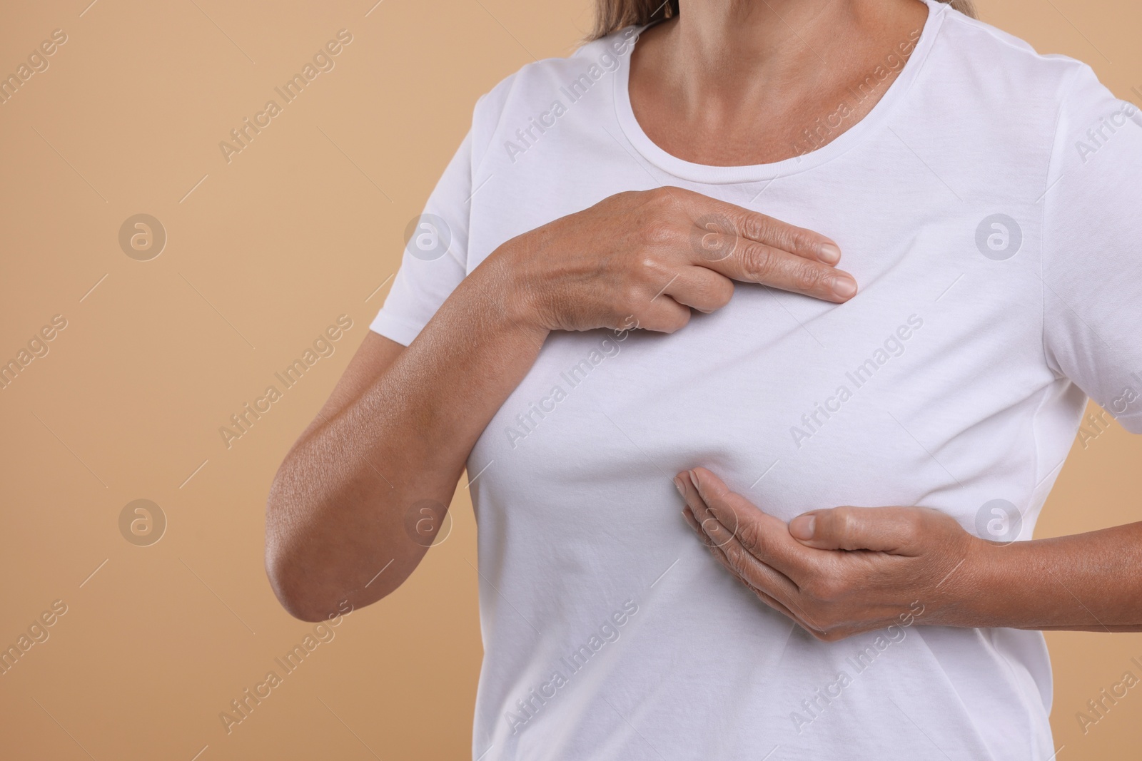 Photo of Woman doing breast self-examination on light brown background, closeup. Space for text