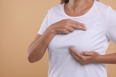 Photo of Woman doing breast self-examination on light brown background, closeup. Space for text