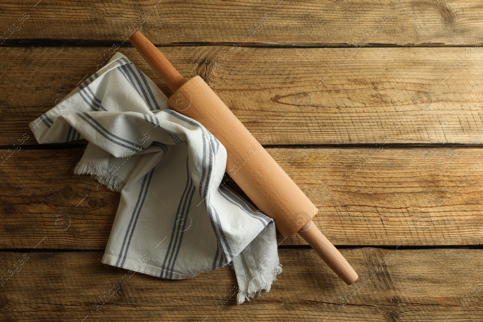 Photo of Rolling pin and kitchen towel on wooden table, top view. Space for text