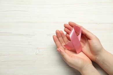 Photo of Breast cancer awareness. Woman with pink ribbon at white wooden table, top view. Space for text